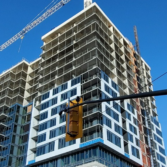 Upward view of apartment building under construction with a crane to the top left, with a yellow street light in the bottom centre of the picture. 
