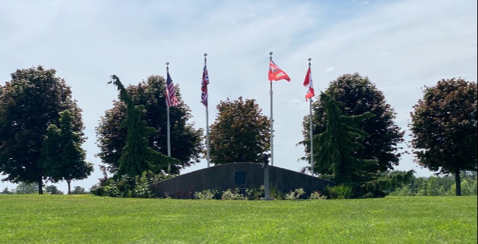 Exterior grass and trees with monument and four flag poles erected for Camp X