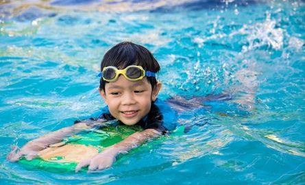 A boy holding a flutter board in a pool