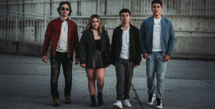 Four Teenagers walking towards camera within a cement area, dressed in dress casual attire.