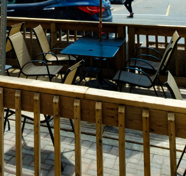 Two streetside patios with guests and a yellow and red umbrella