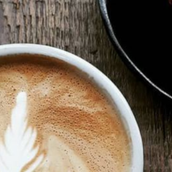 Large view of a latte in a a white cup with a black coffee in the top right corner