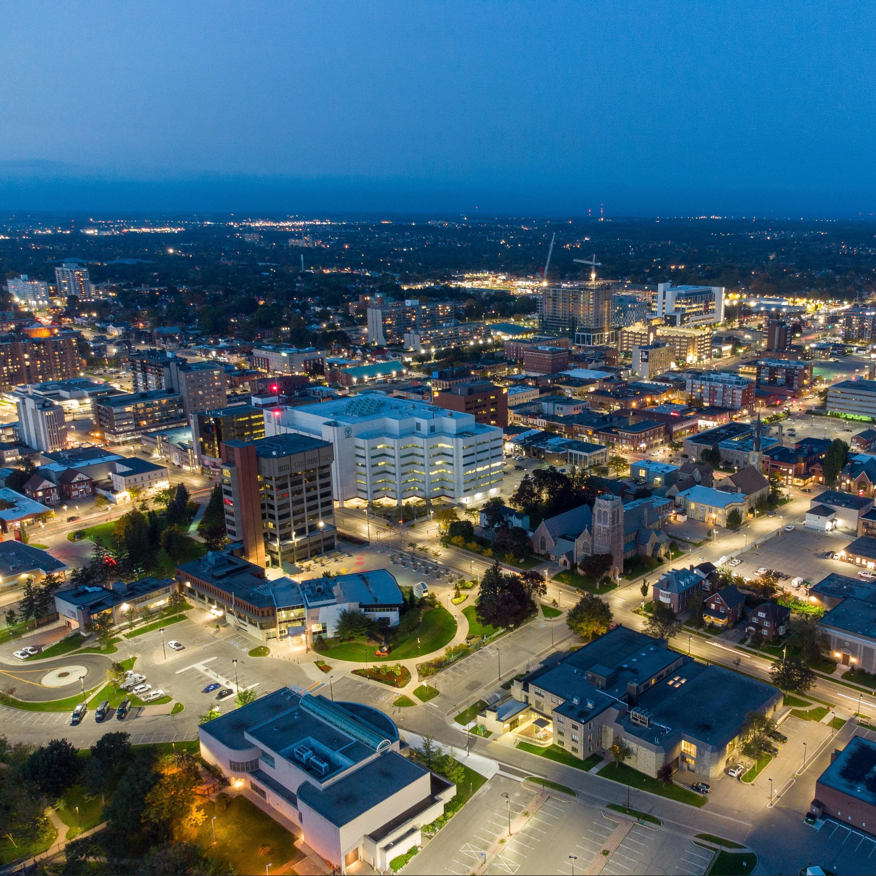 Aerial city shot, with business and street lights glowing and a dark blue sky in the distance