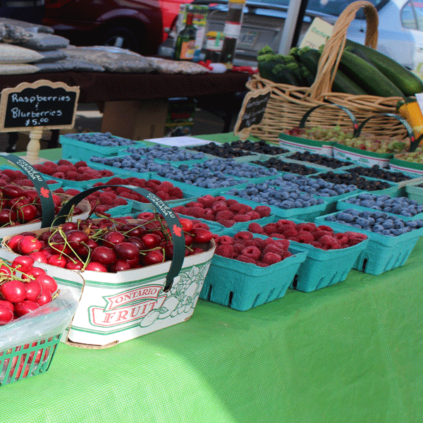 Farmers market green table with cherries, raspberries and blueberries being sold. 