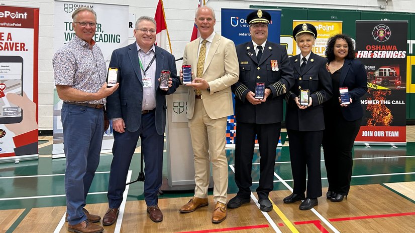 Don Lovisa (Durham College), Dr. Randy Wax (Lakeridge Health), Mayor Dan Carter (City of Oshawa), Fire Chief Derrick Clark (City of Oshawa), Sandra Mackey (DRCISST and City of Oshawa) and Charlene Poranganel (GM and ONStar) stand holding their phones displaying either the PulsePoint Respond or AED app.