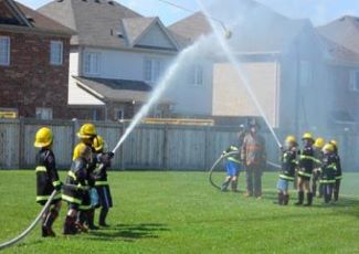 Children in Firefighter gear aiming a fire hose