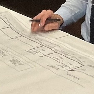 Man in business attire is holding a pen hovering over building sketches 