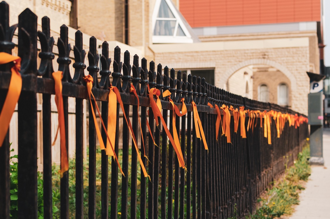 Orange ribbons tied on a wrought iron fence. 