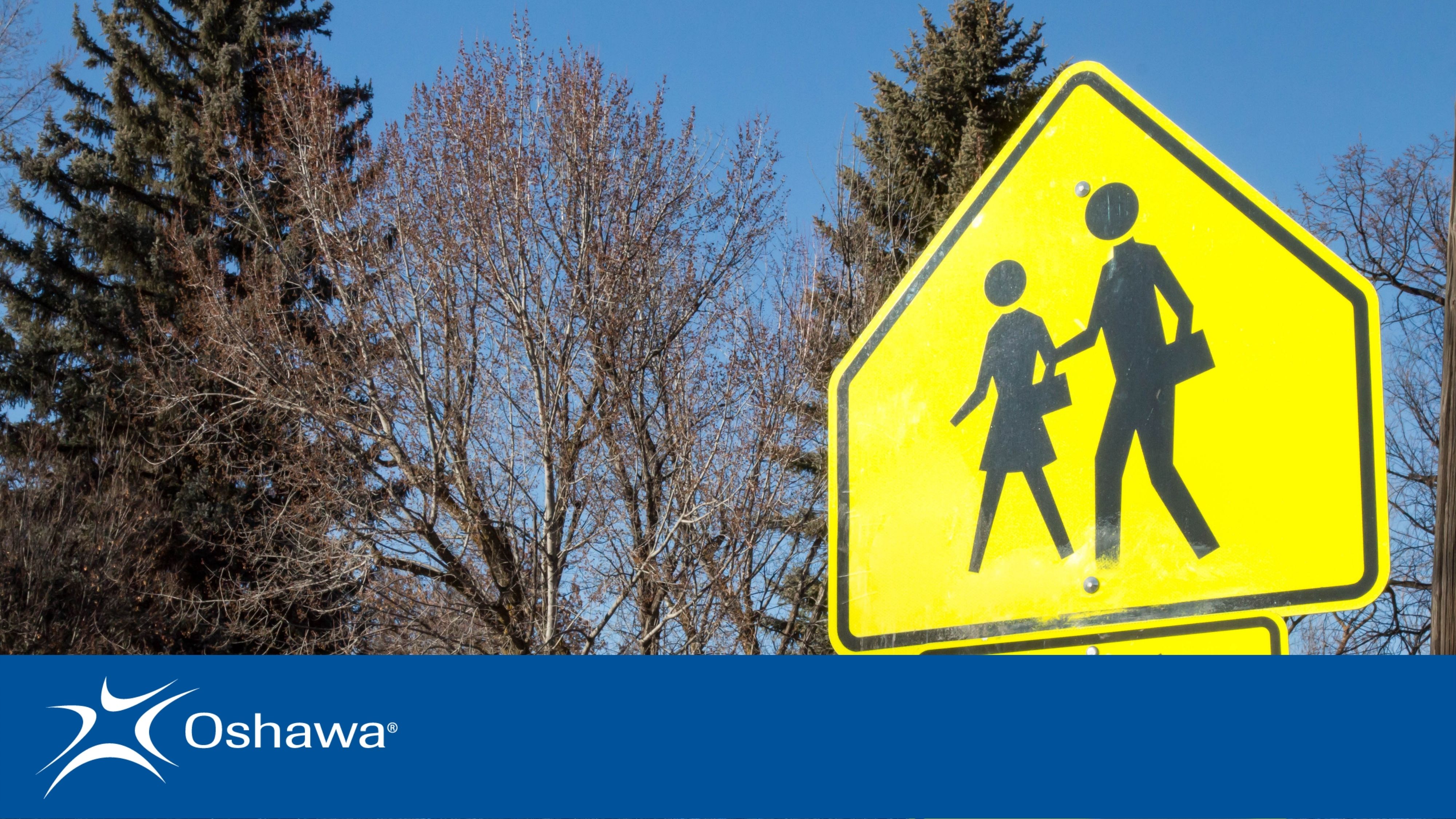 Yellow school crosswalk sign with trees in the background. Blue banner across the bottom with Oshawa logo in the left hand corner.