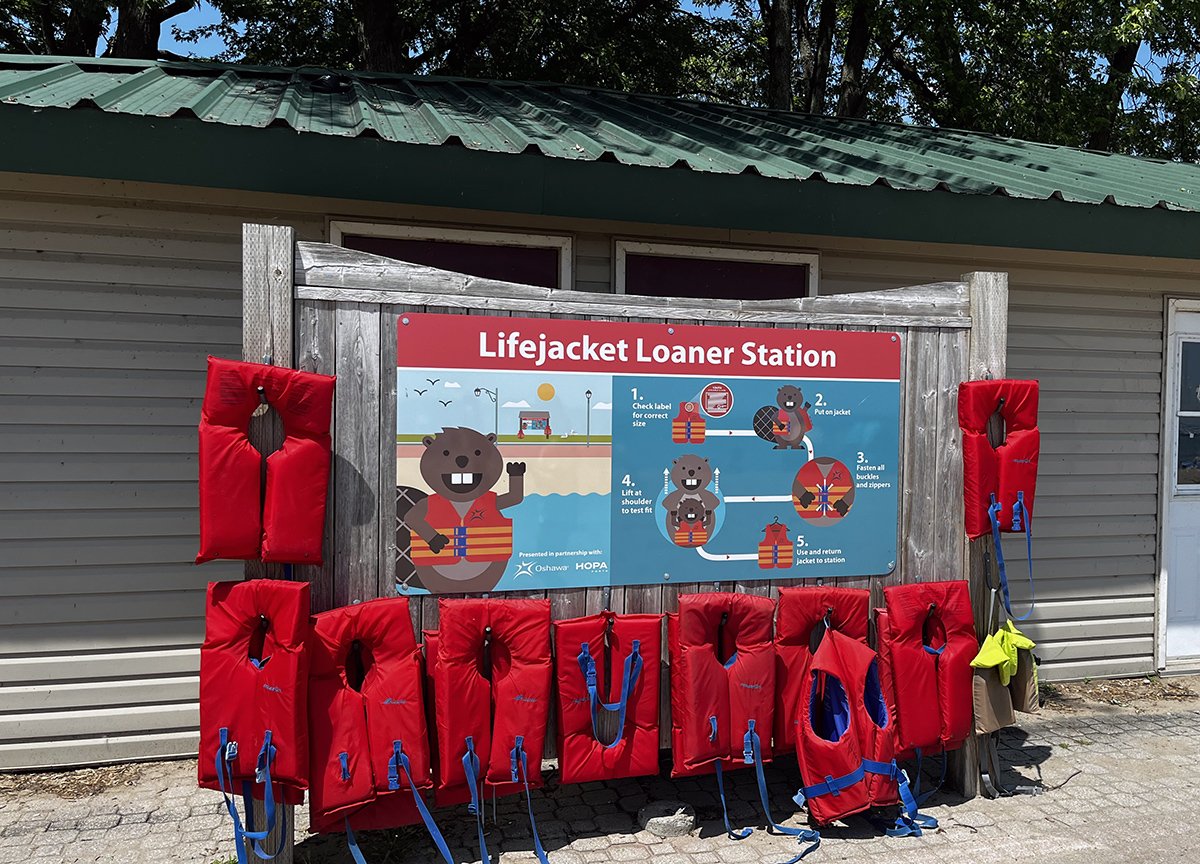 sign promoting the Lifejacket Loaner Program posted on the side of the beach hut at Lakeview Park. Lifejackets hang around the sign. 
