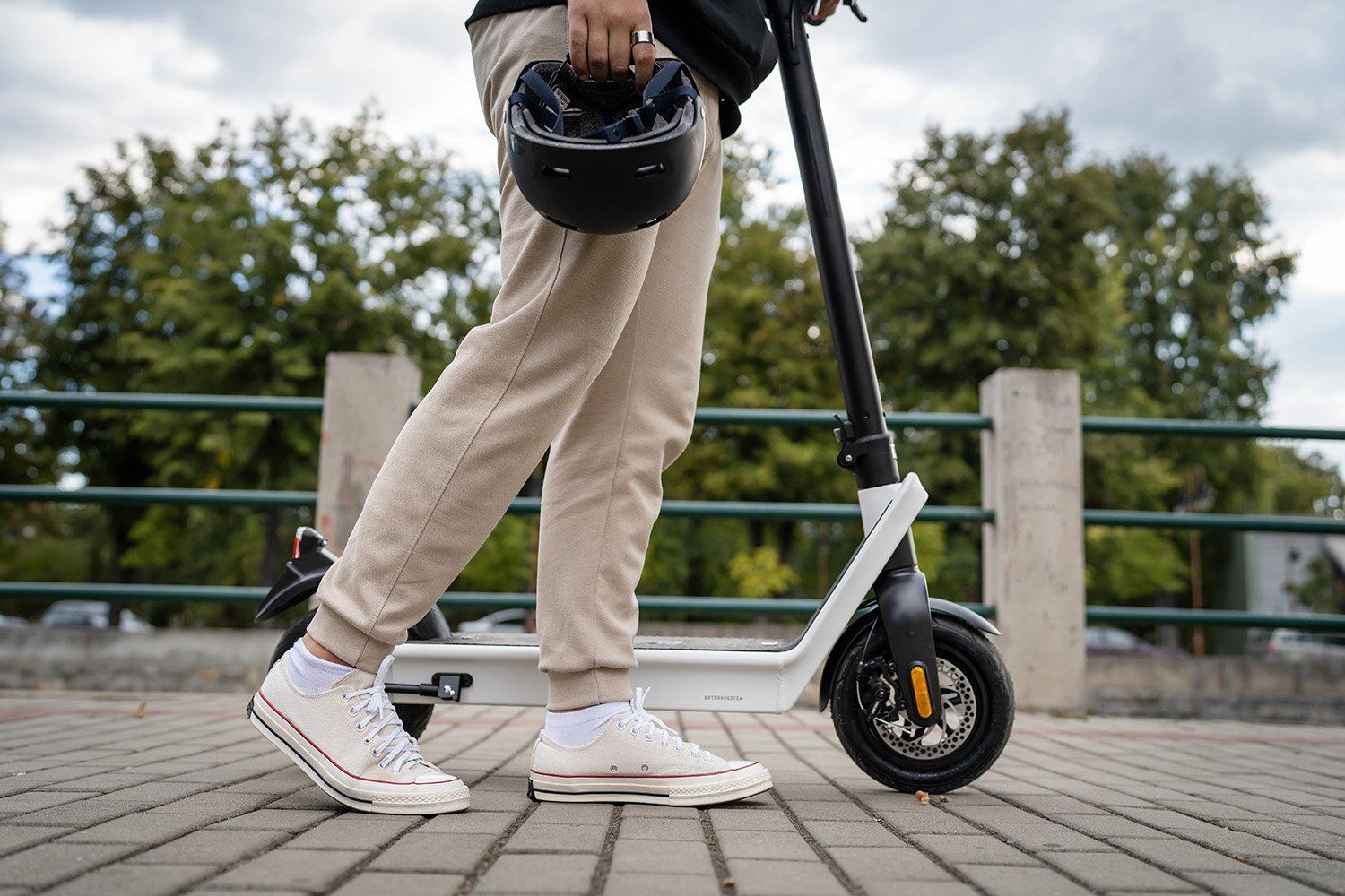 a rider walking an e-scooter and carrying a helmet on a trail or boardwalk