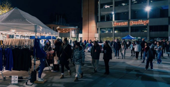 People walking around vendor tent selling clothing, in evening setting