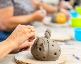 Clay pumpkin sculpture on wood pedestal and hands decorating 