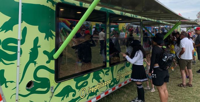 Side trailer with awnings and windows, small reptiles inside, people peeking in.
