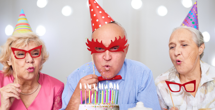 3 older people blowing out candles on a cake