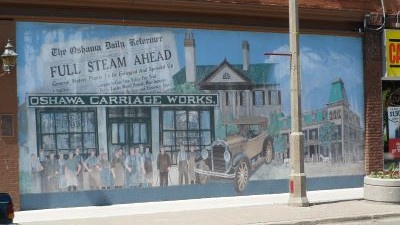 The mural is two panels depicting a scene by water and the storefront of McLaughlin Carriage Works.