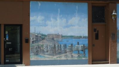 The mural is two panels depicting a scene by water and the storefront of McLaughlin Carriage Works.