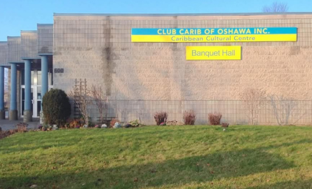 Exterior grey brick building with side main entrance view, Club Carib of Oshawa signage hung high on building.
