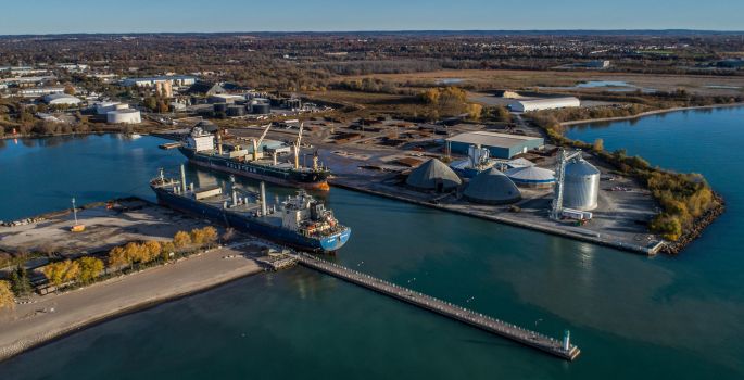 Ariel photo of Oshawa waterfront with large ship in dock, pier and various buildings on land surrounding port