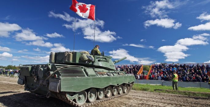 Military tank with Canadian flag parked in stadium in front of bleachers with spectators onlooking