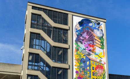 Top portion of oversize mural mounted on side of parking garage, colourful.