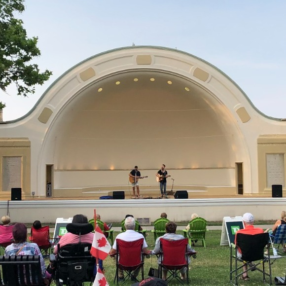 Two musicians playing in bandshell with audience on the lawn in front