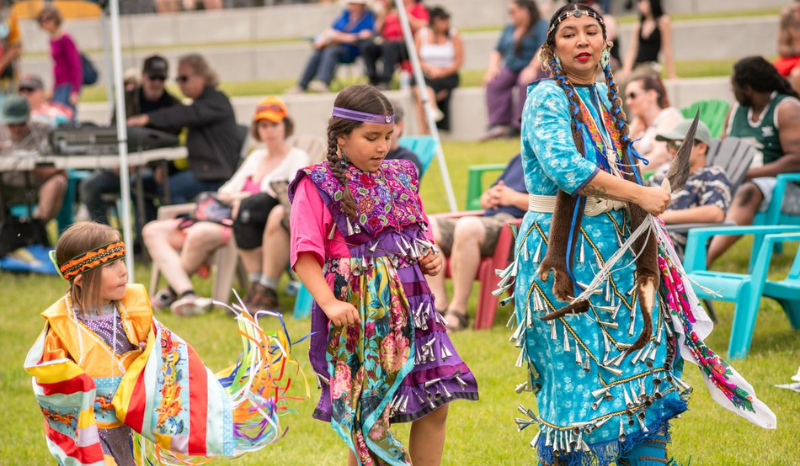 Indigenous Mother and two children dancing in traditional Indigenous Regalia clothing