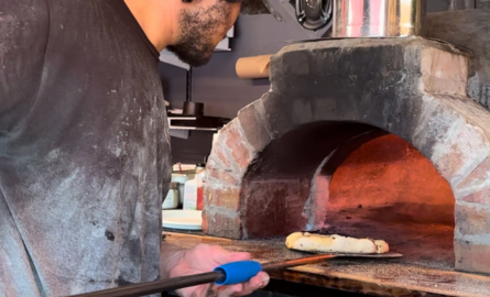 Man putting homemade pizza into a wood burning stove.