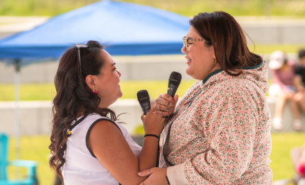 Two indigenous women facing one another with microphone, singing.