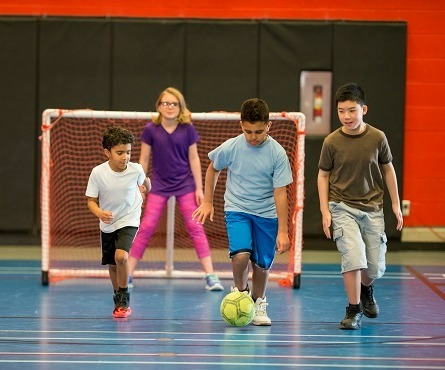 Four kids playing soccer in a gymnasium