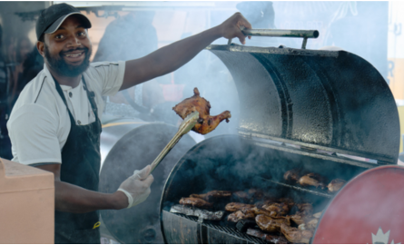 Food vendor at a BBQ showing a cooked chicken leg