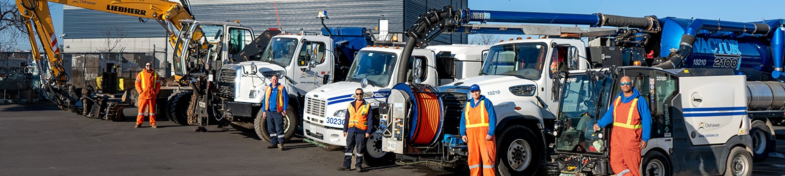 5 different types of City trucks parked in a row with City workers standing in front