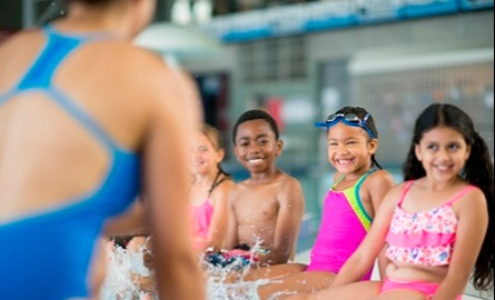 Kids sitting on the side of a pool looking at an instructor