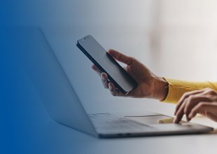 Right hand holding a cell phone, left hand touching laptop