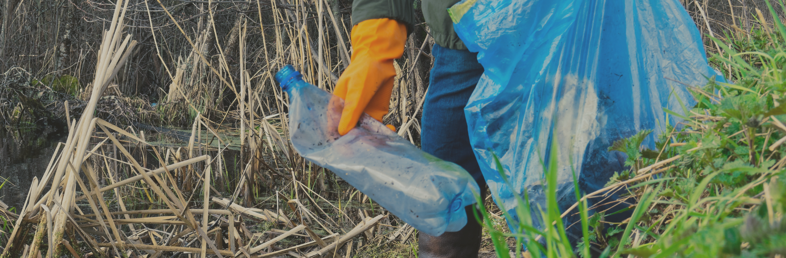 hand in orange rubber glove picking up empty plastic waterbottle off of the ground