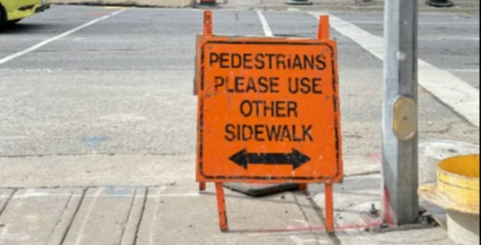 an orange sign telling pedestrians the sidewalk is closed