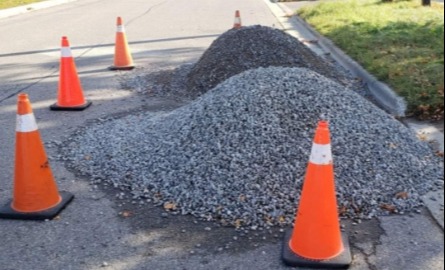 Five orange cones around a pile of gravel on the roadway 
