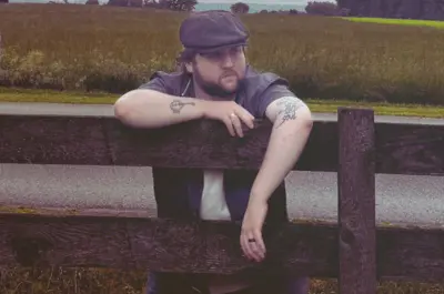 man leaning over wooden fence by road