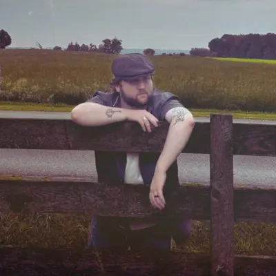 man leaning over wooden fence by road
