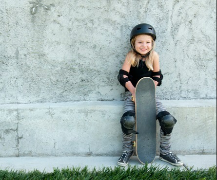 Young girl with skateboard leaning against wall