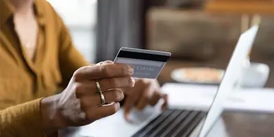 A person holding a credit card in front of a laptop