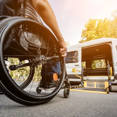 person in wheelchair approaching white van with accessible ramp