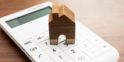 Wooden house token sitting on top of a white calculator