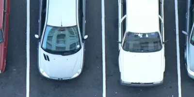 aerial view of a silver and a white car in parking spaces