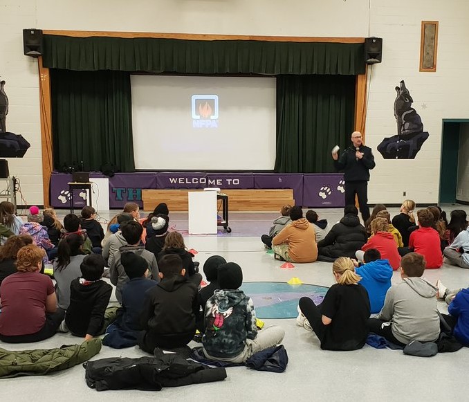 Fire prevention inspector presenting in front of children in a school audittorium