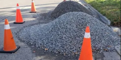 pile of gravel on road with orange pilons around it