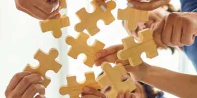 multiple hands in the circle holding large puzzle pieces