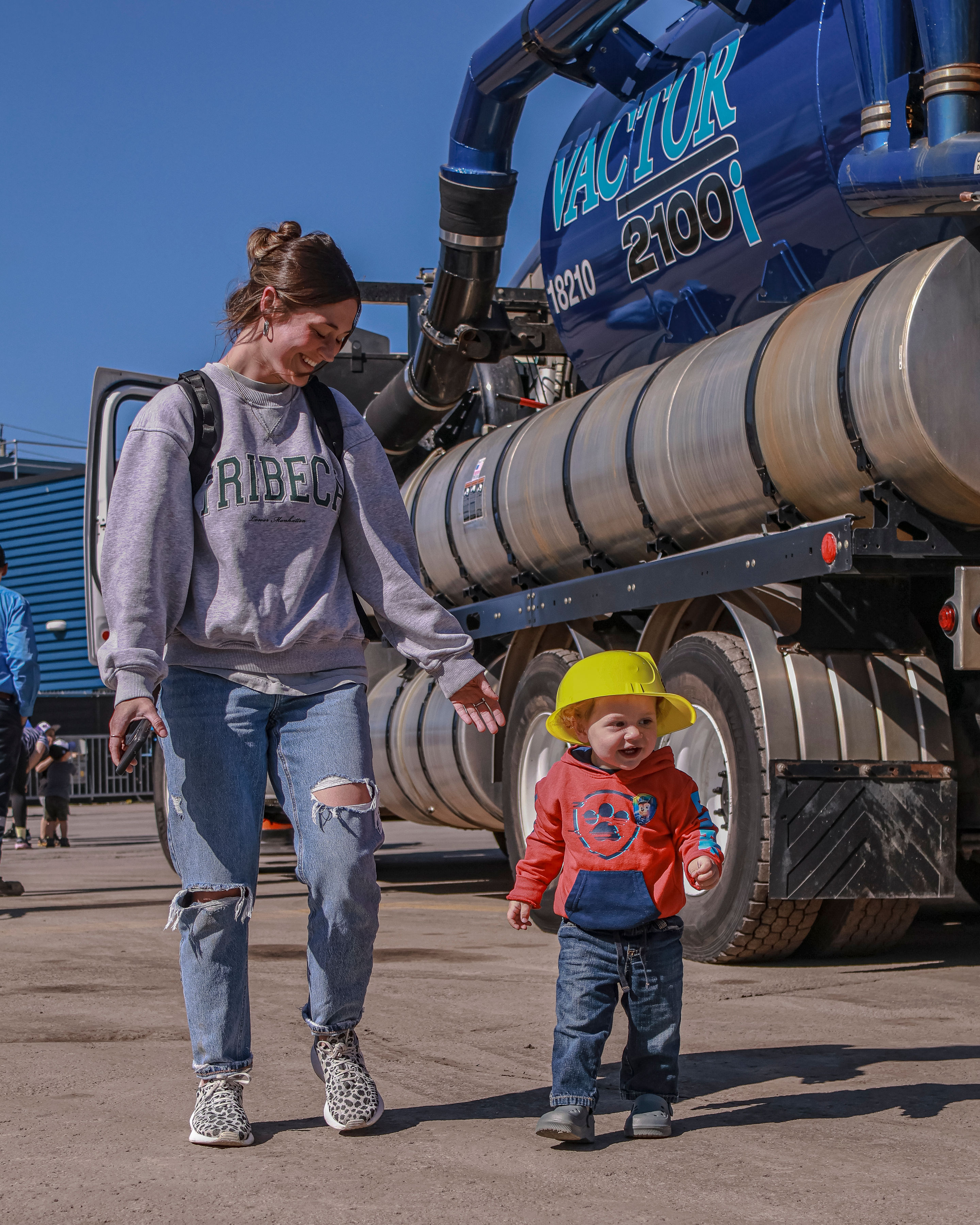 toddler walking beside his mom in front of vactor truck