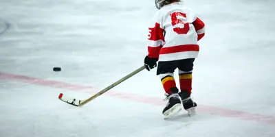 Child on ice carrying stick approaching puck