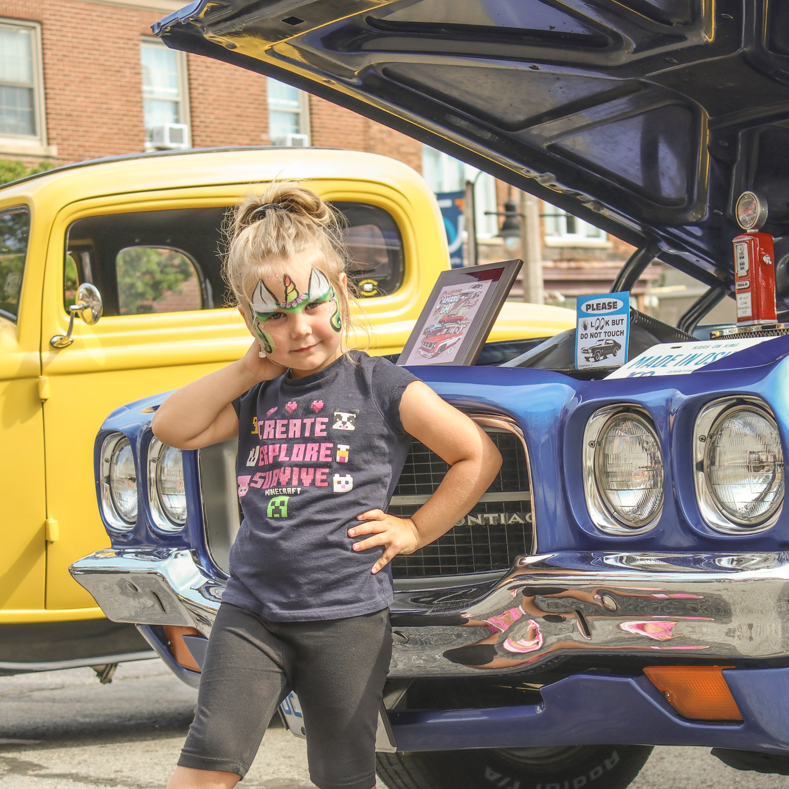 girl with face paint standing in front of classic cars